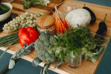 A vibrant display of fresh vegetables and fruits on a wooden board, including bell pepper, cabbage, and more.